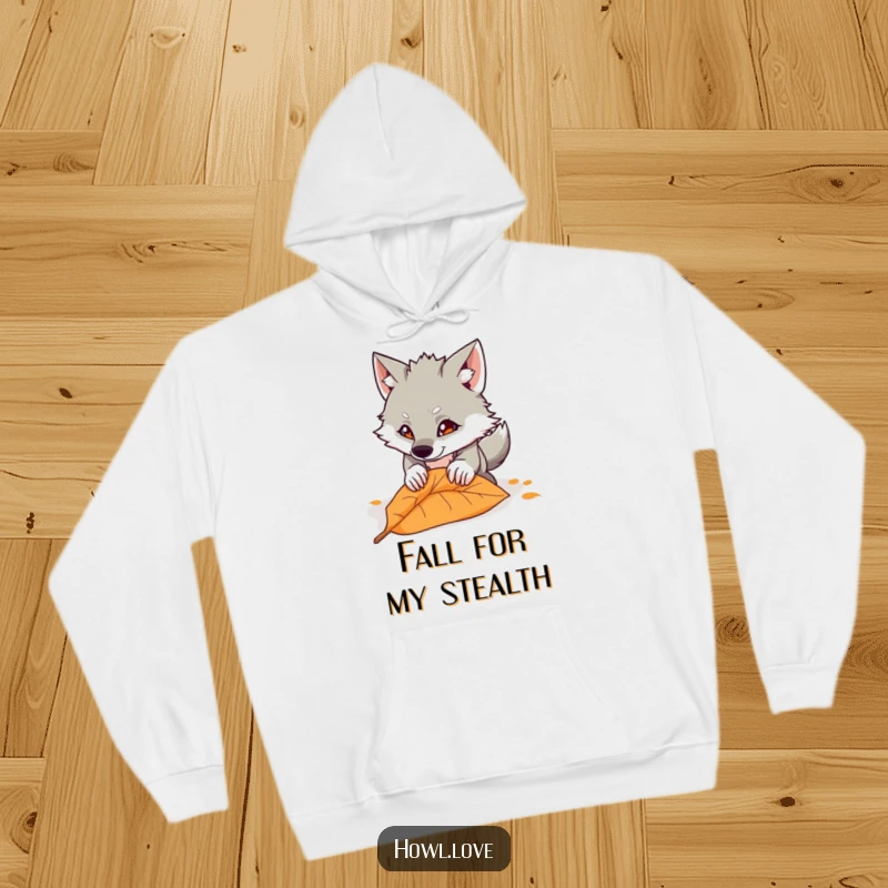 Funny hoodie showcasing a mischievous wolf cub in mid-air, playfully pouncing down towards a brown fallen leaf. Cozy and comical.